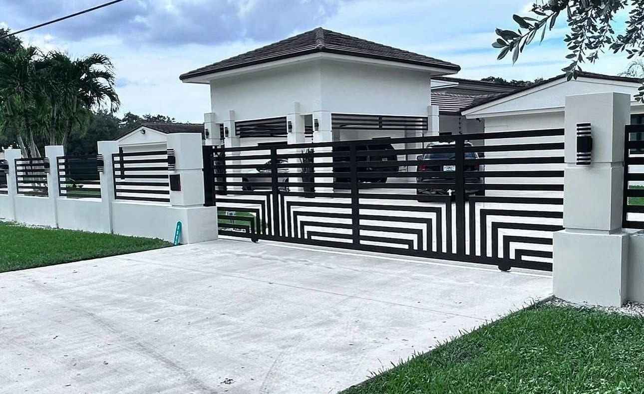 Sliding driveway gate with a black and white geometric slat pattern and matching fence, built by J & M at a modern home