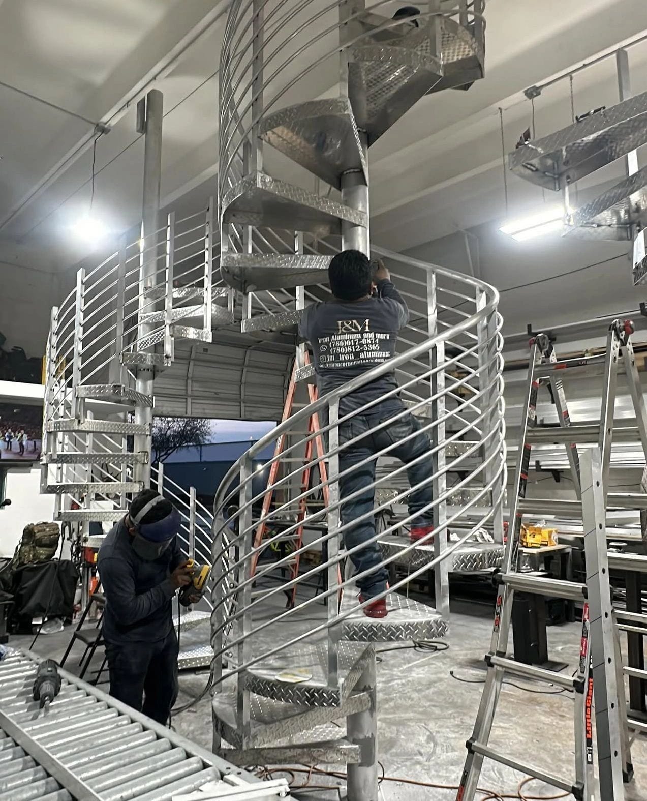 J & M crew in company shirts building an aluminum spiral staircase inside the shop